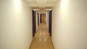 A long, narrow hallway with light-colored walls and wooden flooring, leading to a door at the end. - Hotel Palak Palace (Ahmedabad)