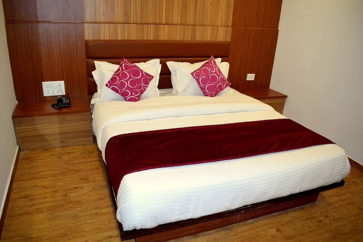 Ein Hotelzimmer mit einem Holz-Kopfteil, einem Bett mit weißer Bettwäsche und zwei roten Kissen, einem Nachttisch aus Holz mit einem Telefon und einer roten Tagesdecke.