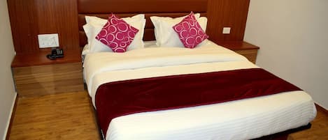 A hotel room with a wooden headboard, a bed with white bedding and two red pillows, a wooden nightstand with a phone, and a red throw blanket.