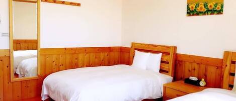 A room with two wooden beds, a wooden nightstand with a clock, and a painting of sunflowers on the wall.