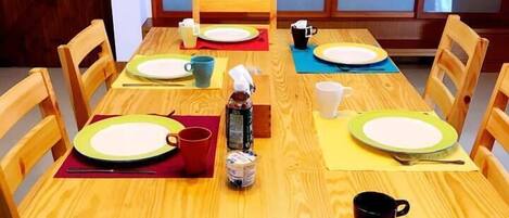 A dining table set with plates, cups, and a bottle, surrounded by chairs.