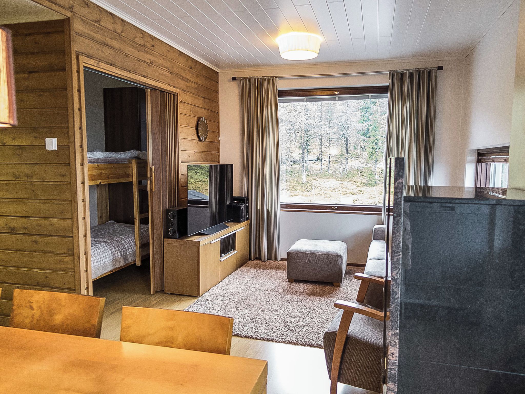 Ein kleines Zimmer mit Etagenbett, Fernseher, Tisch und einem Fenster mit Vorhängen.
