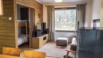 Een kleine kamer met een stapelbed, een televisie, een tafeltje en een raam met gordijnen.