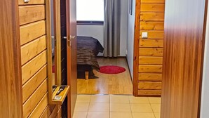 Un pasillo estrecho con paneles de madera que conduce a un dormitorio con cama, cortinas y una alfombra roja.