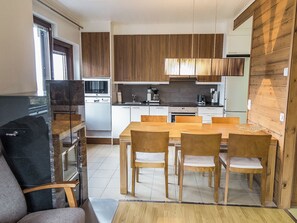 A compact kitchen with wooden cabinets, a dining table with chairs, and a refrigerator.
