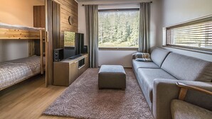 Una habitación pequeña con una cama litera, televisión, sofá y ventana con persianas.