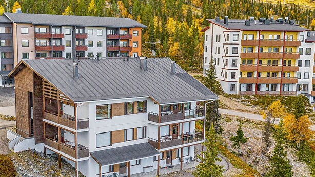 Un edificio moderno de varios pisos con balcones, techo plano y vistas a un paisaje montañoso.