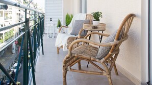 A balcony with wicker furniture, a potted plant, and a view of the street below. - Modern Bohemian Style Sun-Splashed Loft (Athens)