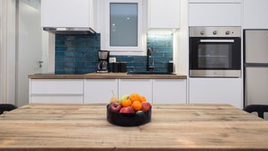 A modern kitchen with a wooden table, a fruit bowl, and stainless steel appliances. - Modern Bohemian Style Sun-Splashed Loft (Athens)