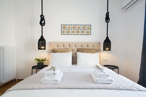 A neatly made bed with white linens and two towels, a tufted headboard, and a wall-mounted decorative piece above. - Modern Bohemian Style Sun-Splashed Loft (Athens)