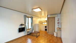 A compact living space with a kitchenette, a flat-screen TV mounted on the wall, a small table with a cup, and a wooden floor.