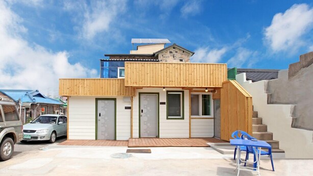 A modern two-story house with a wooden exterior, a visible garage door, and a staircase leading to the upper level.
