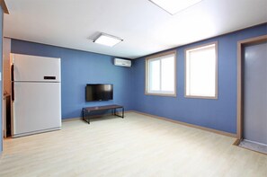 A room with a white refrigerator, a flat-screen TV, a bench, and two windows with blinds. - Brothers Pension (Sokcho)