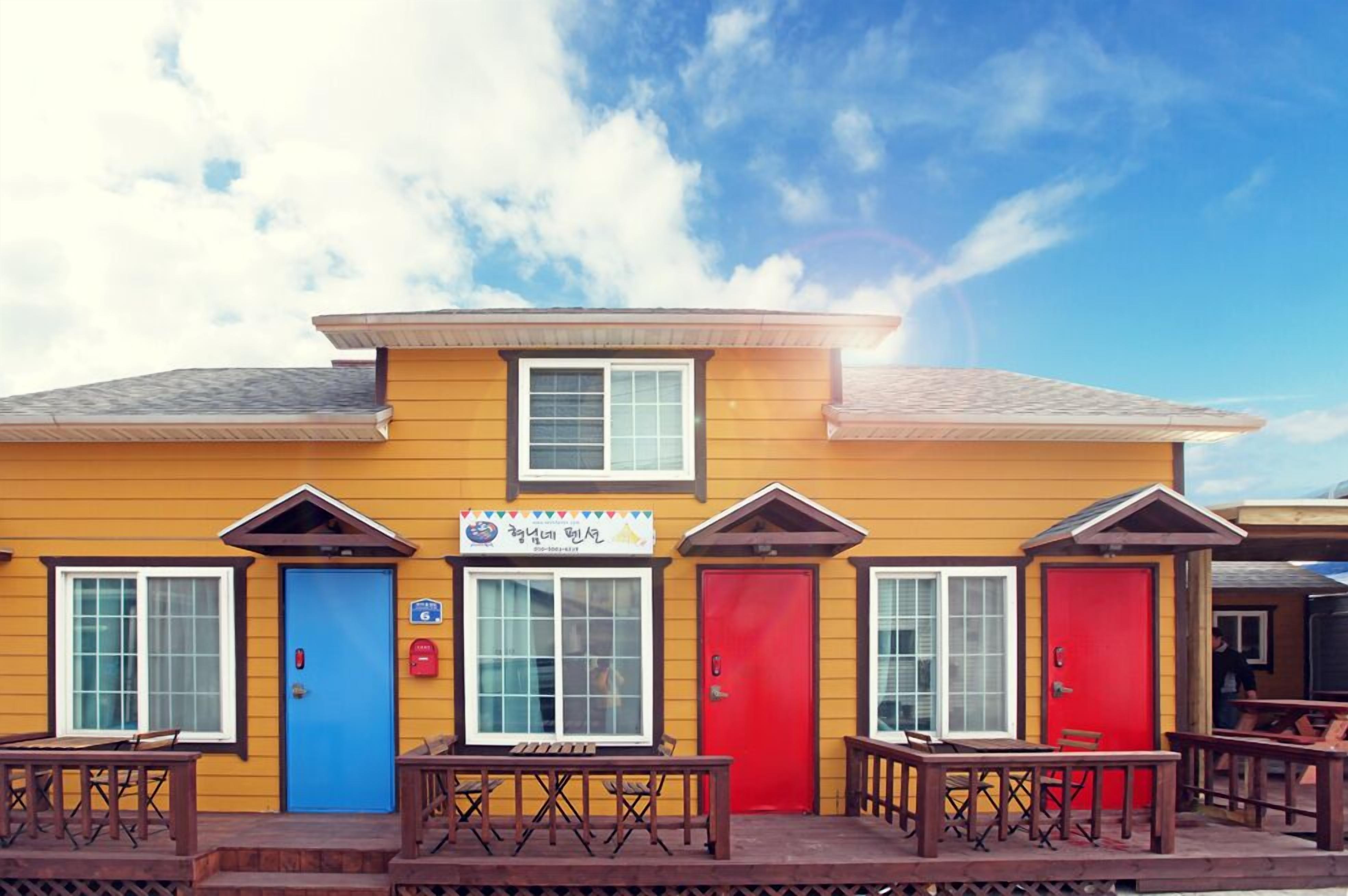 Uma fileira de cabanas coloridas, com portas azuis e vermelhas, uma placa acima da entrada e área de estar externa.
