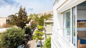 Un immeuble d’habitation doté d’un balcon, donnant sur une rue où sont garées des voitures, et offrant une vue lointaine sur un bâtiment historique.