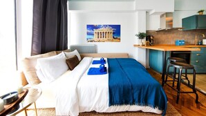 Une chambre d’hôtel moderne équipée d’un lit, d’un petit bureau, d’un coin cuisine et d’une grande fenêtre avec des rideaux.