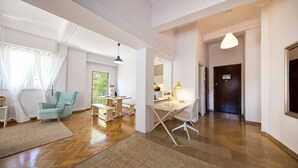 Une pièce spacieuse dotée d’un plancher en bois, d’un coin repas avec une table et des chaises, d’un canapé et d’une grande fenêtre agrémentée de rideaux.