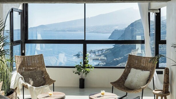 A room with a large window, two wicker chairs, a small table, and a potted plant.