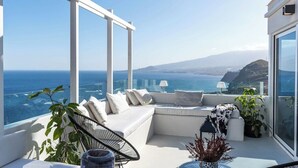 A balcony with a white sofa, a chair, and a table with a vase.