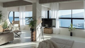 A modern living room with a large flat-screen TV, comfortable seating, and a view of the sea.