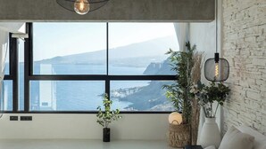 A modern living room with a large window, a sofa, a plant, and a hanging light fixture.