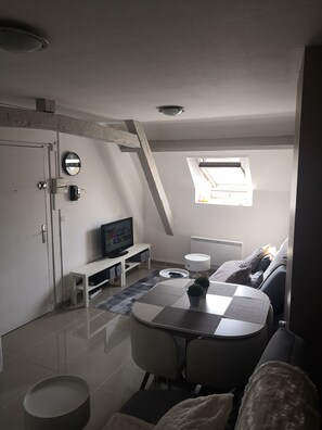A compact living space with a TV, a small dining table, a sofa, and a window with natural light. - Cozy village ......... (Bonneuil-en-France)