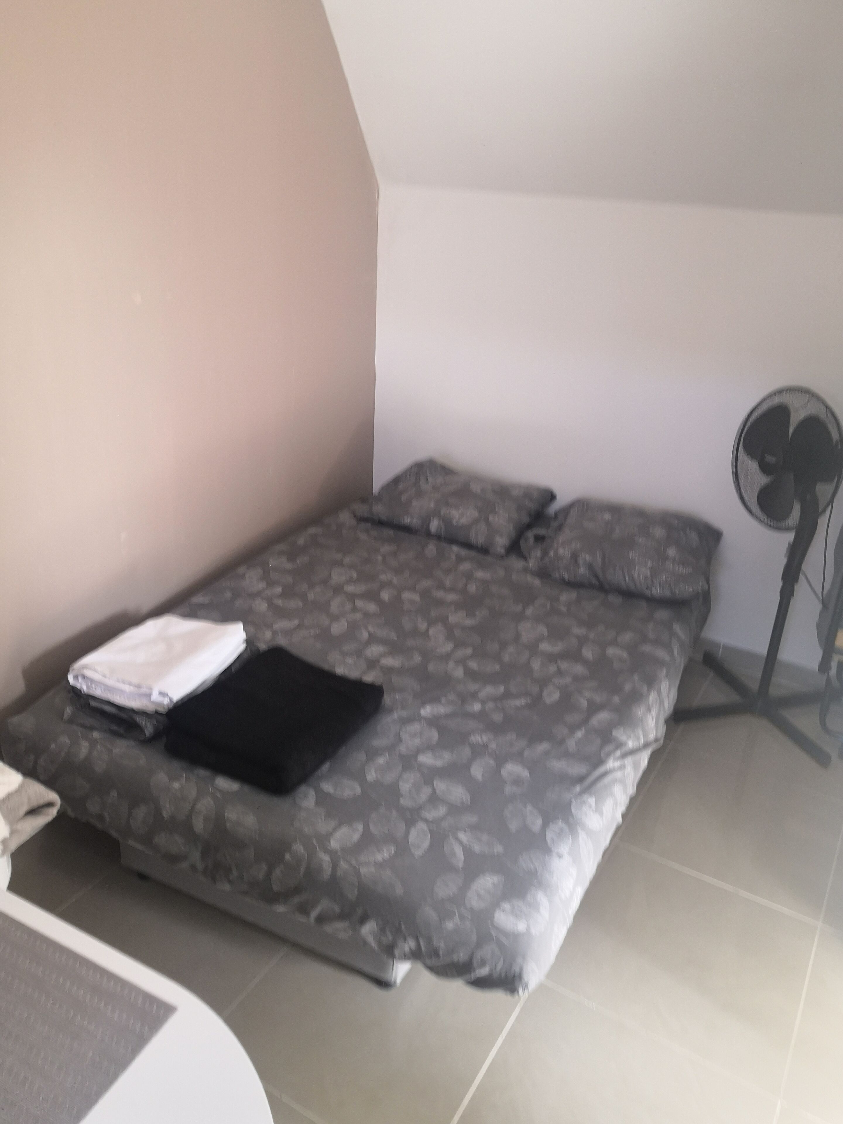 Un lit bien fait, avec une couvre-lit à motifs, des oreillers et un vêtement blanc plié posé sur le lit.