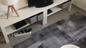 Moderni olohuone, jossa on valkoinen, litteänäyttöinen televisio, kaksi lattiavalaisinta ja harmaa matto.