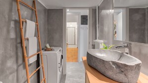 A modern bathroom with a stone sink, a wooden ladder, and a washing machine.