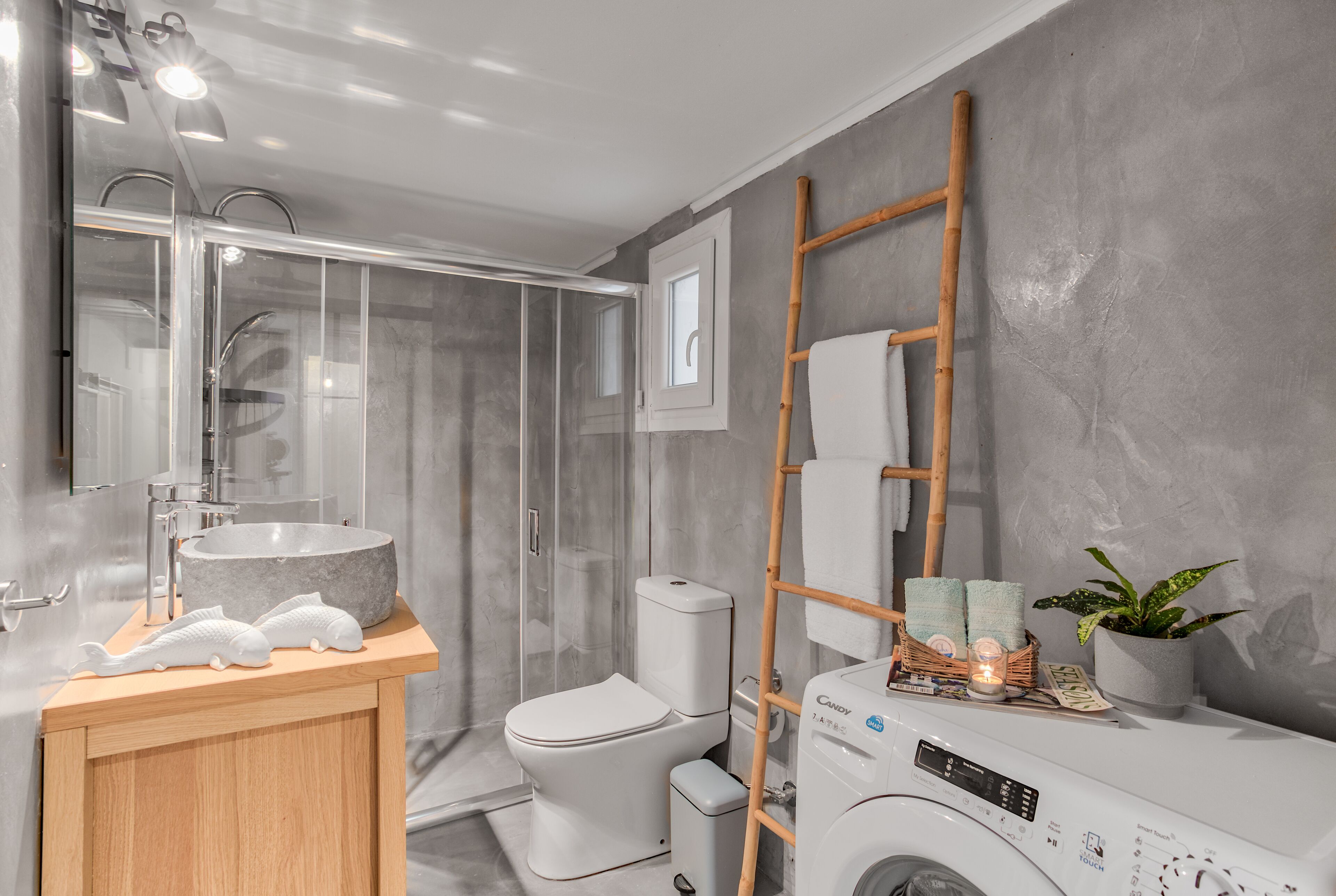 Une salle de bain moderne avec une douche à parois de verre, un meuble-lavabo en bois, un lave-linge et un escabeau en bambou.