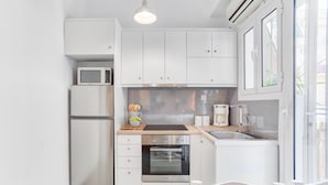 A compact kitchen with white cabinetry, a microwave, a refrigerator, a built-in oven, a coffee maker, and a wooden countertop.