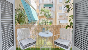 A small outdoor seating area with two white chairs and a table, surrounded by a bamboo fence and plants.