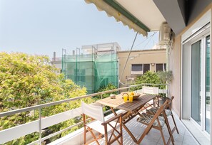 A balcony with a wooden table, chairs, and a potted plant. - Sun splashed sanctum balconies Acropolis (Athens)