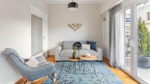Ett modernt vardagsrum med en grå soffa, en blå fåtölj, ett soffbord och ett stort fönster med utsikt över byggnader och grönska.