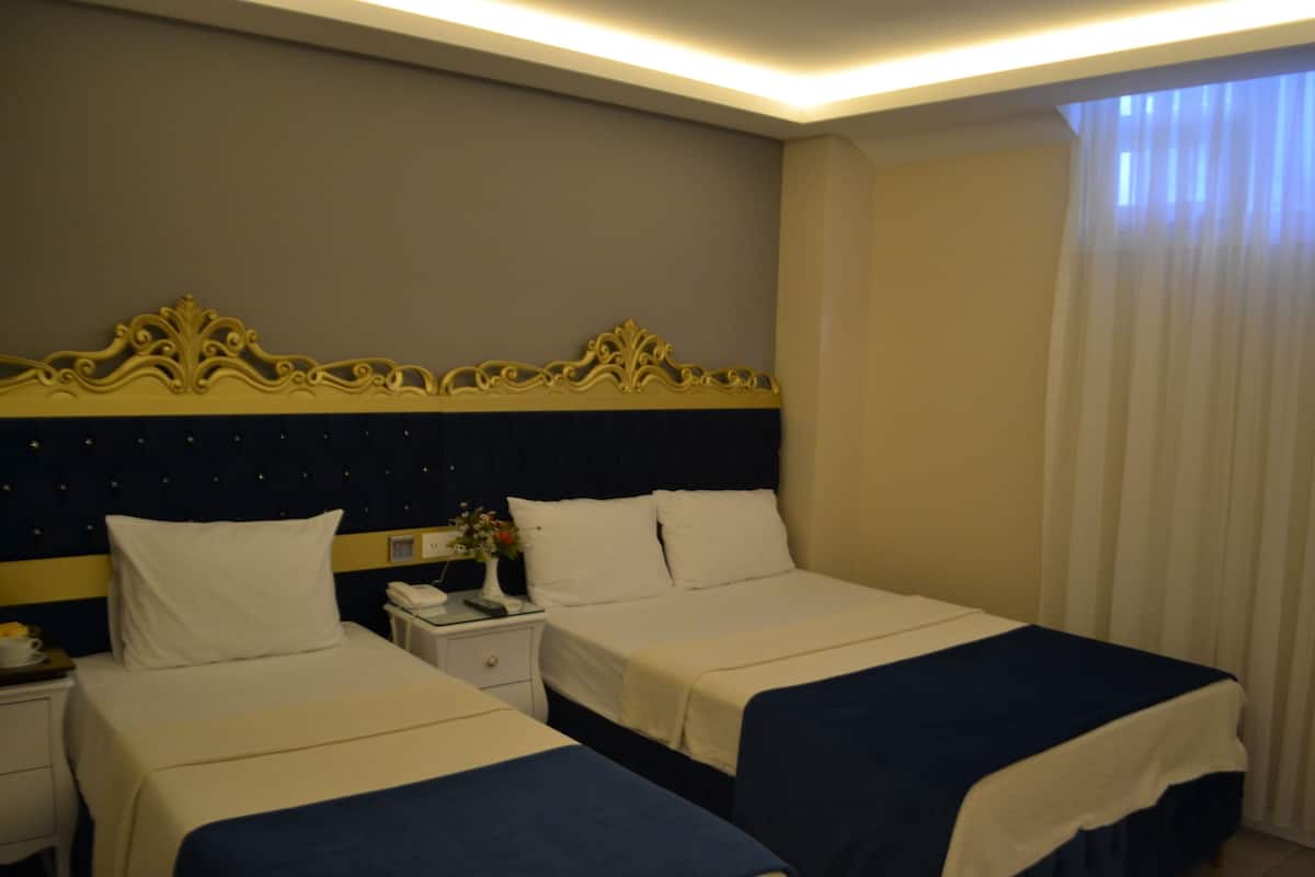 Une chambre d’hôtel avec deux lits, une table de chevet avec un téléphone et un vase, et une tête de lit décorative.