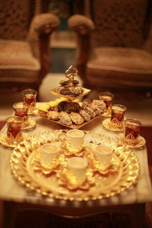 A table with trays of pastries and glasses of tea, set in a room with patterned chairs. - Constantinopolis Hotel (Istanbul)