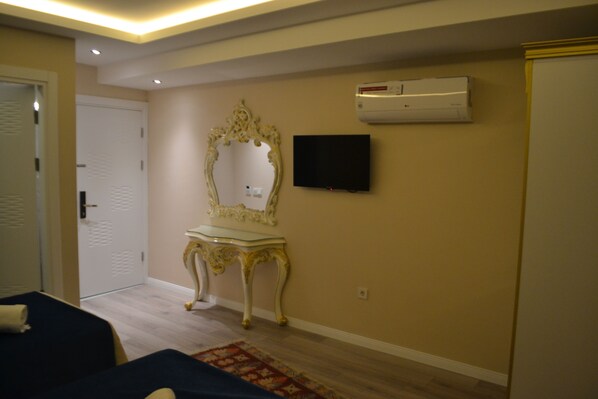 Habitación de hotel con cama, tocador con espejo, televisor de pantalla plana y unidad de aire acondicionado en la pared.