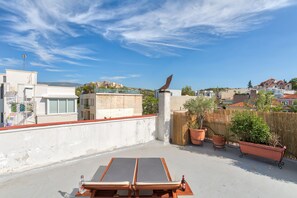 Terraço no telhado com duas cadeiras de lounge, uma mesa e plantas em vasos.