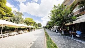 A cobblestone street lined with outdoor seating and greenery, leading to a building with a storefront. - Serene Acropolis View Roofdeck (Athens)