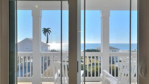 A balcony with white chairs, a view of the ocean, and a palm tree. - Anita Getaway: Charming 4-bedroom home in Oak Island with ocean views and private pool. (Oak Island)
