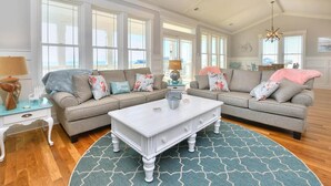 A spacious living room with two sofas, a coffee table, and a large window providing a view of the ocean. - Anita Getaway: Charming 4-bedroom home in Oak Island with ocean views and private pool. (Oak Island)