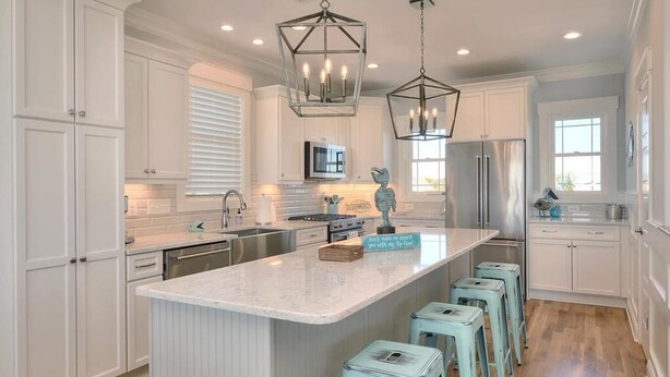 A kitchen with white cabinetry, a central island with stools, stainless steel appliances, and pendant lighting. - Anita Getaway: Charming 4-bedroom home in Oak Island with ocean views and private pool. (Oak Island)