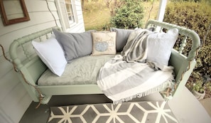 A vintage-style porch with a cushioned bench, patterned cushions, and a decorative throw blanket. - Chickadees Cottage and Pottery - centrally located, private comfortable cottage. (Arden)