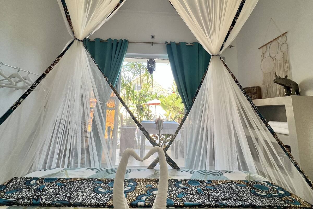 Una habitació amb un llit, cortines blanques, vista exterior i un cigne decoratiu al llit.
