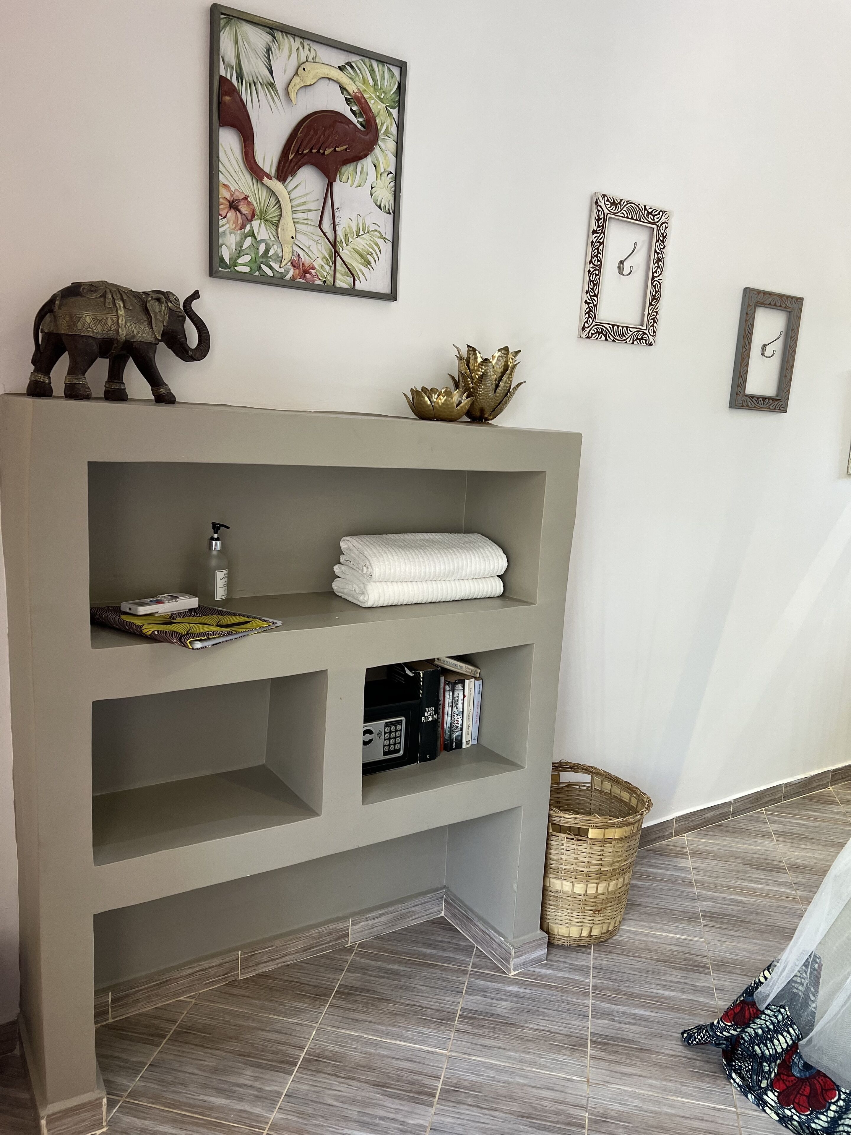 A room with a grey console table, a wall-mounted elephant decoration, a framed artwork of a flamingo, and a wicker basket on the floor.