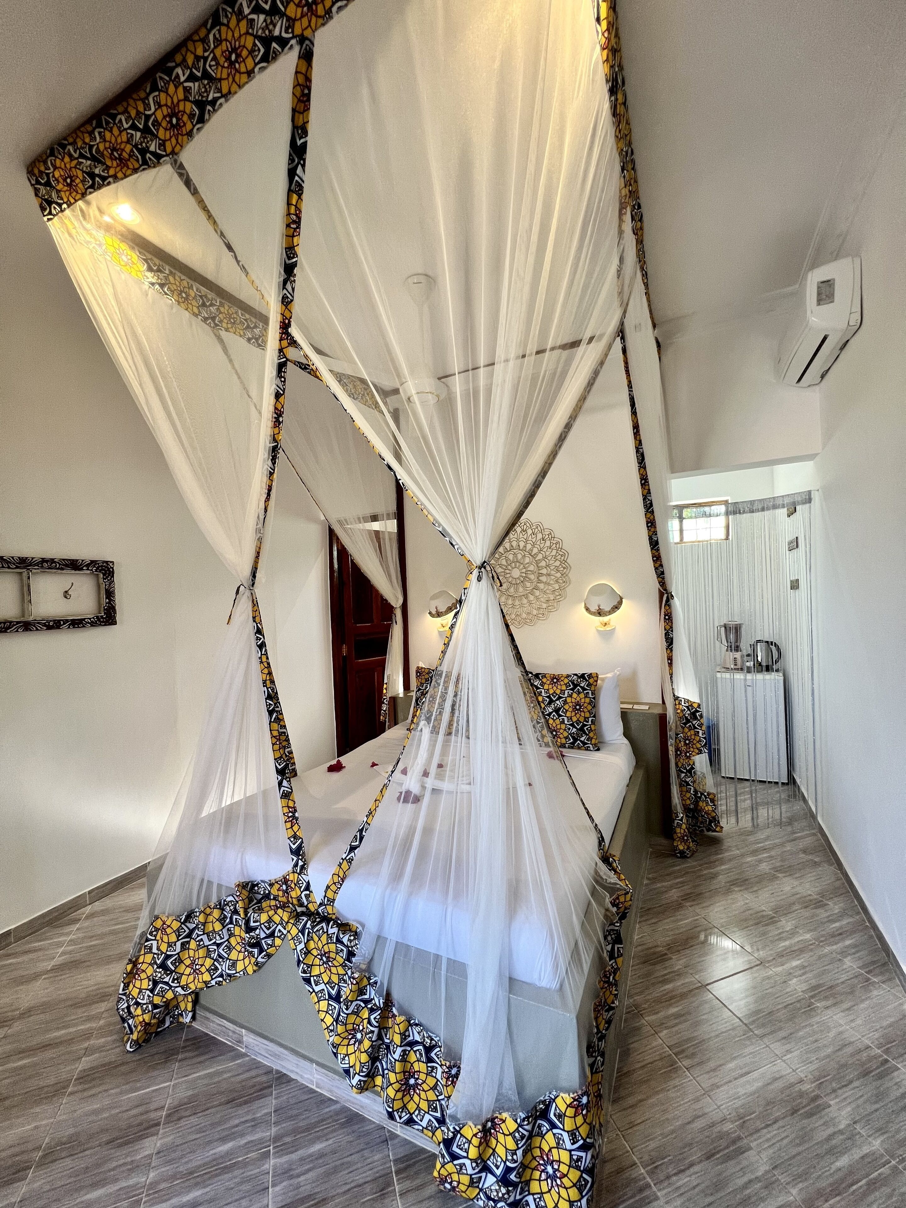 Un dormitorio con cama con dosel, una mesita de noche, un espejo y una puerta que da a otra habitación.