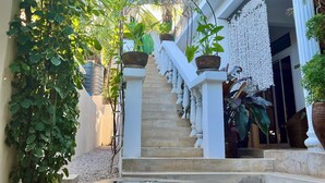 A staircase leading to a balcony with white columns, surrounded by greenery and a water feature. - Gadea Boutique Hotel (Jambiani)