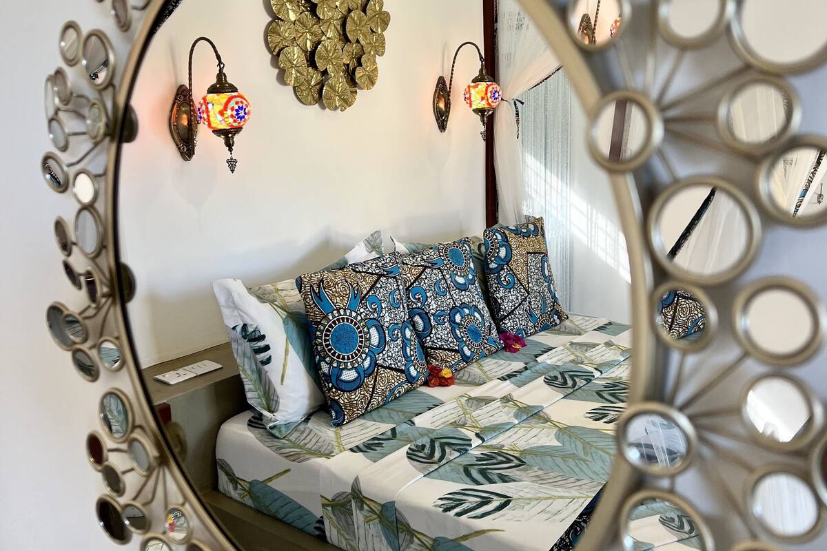Un llit amb roba de llit estampada, un penjoll decoratiu i llums subjectes a la paret.