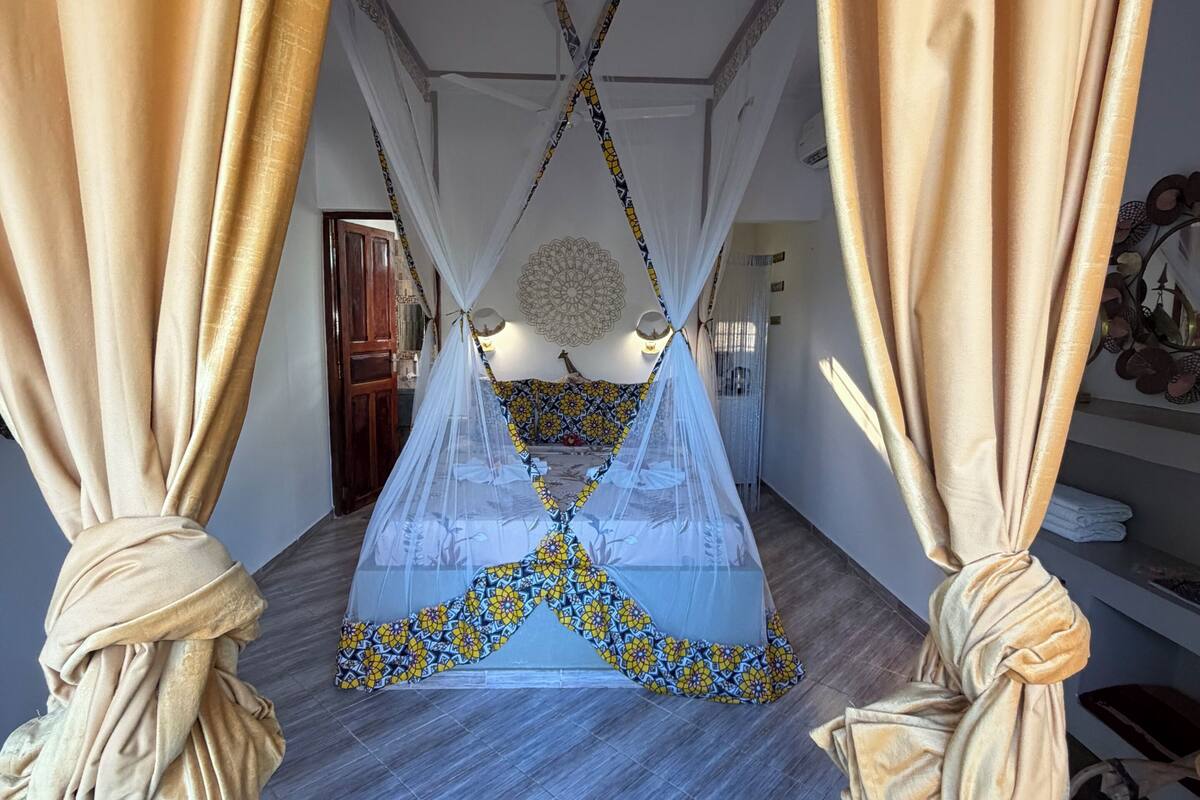 Habitació amb un llit sota una estructura de teules, una catifes amb motius i un aplacament decoratiu al sostre.