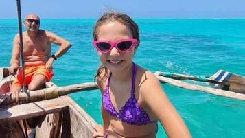 Una persona con traje de baño morado sentada en un bote de madera, con agua turquesa transparente al fondo.